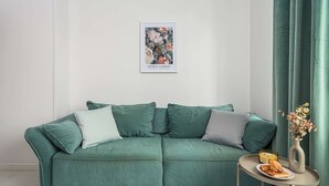 En tealgrøn sofa med puder, et lille bord med et lys og en vase, samt et indrammet kunstværk på væggen.