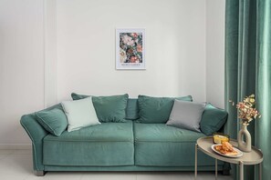 Ein saphirblaues Sofa mit Kissen, ein kleiner Tisch mit Kerze und Vase sowie ein gerahmtes Kunstwerk an der Wand.