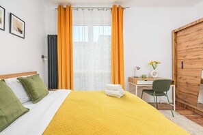 A hotel room with a bed, a desk, a chair, a wardrobe, and a window with curtains. - Warsaw Apartment for 6 with Parking (Warszawa 2)