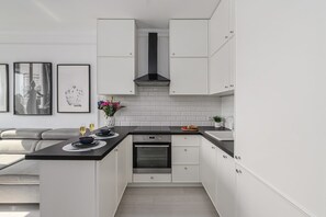 A modern kitchen with white cabinetry, a black countertop, and a built-in oven. - Flat with Quiet Courtyard (Warszawa)