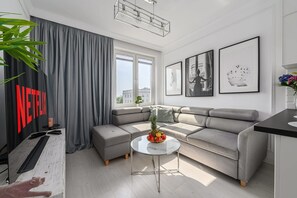 A modern living room with a grey sectional sofa, a glass coffee table with fruit, and a large window with curtains. - Flat with Quiet Courtyard (Warszawa)
