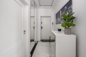 A hallway with white doors, a potted plant, and a cityscape painting on the wall. - Flat with Quiet Courtyard (Warszawa)