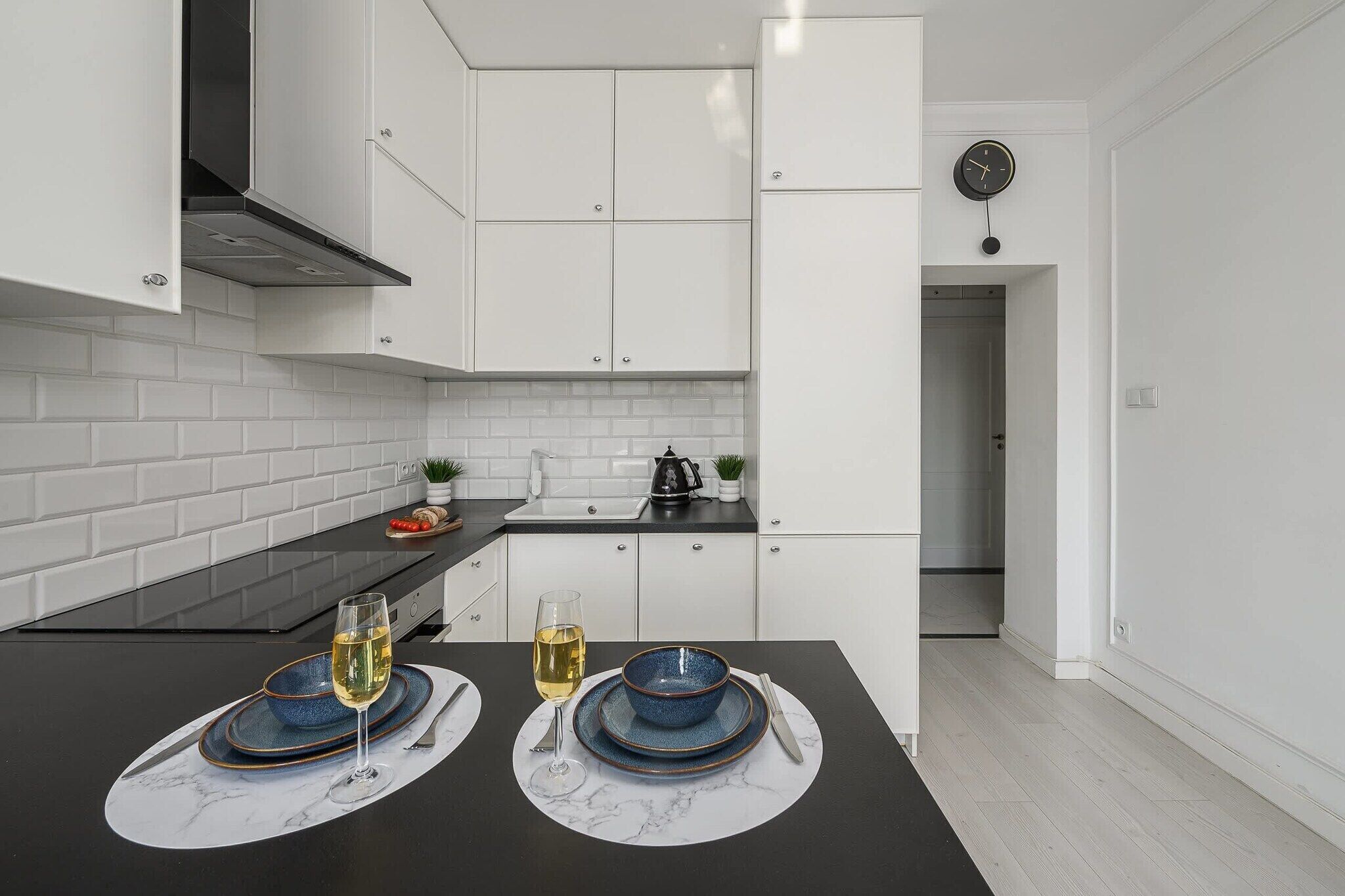 Uma cozinha moderna com armários brancos, bancada preta e um espaço de refeições com dois pratos azuis e copos.