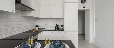 Uma cozinha moderna com armários brancos, bancada preta e um espaço de refeições com dois pratos azuis e copos.