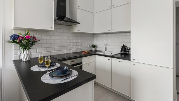 Una cocina moderna con armarios blancos, encimera negra y campana extractora de acero inoxidable.