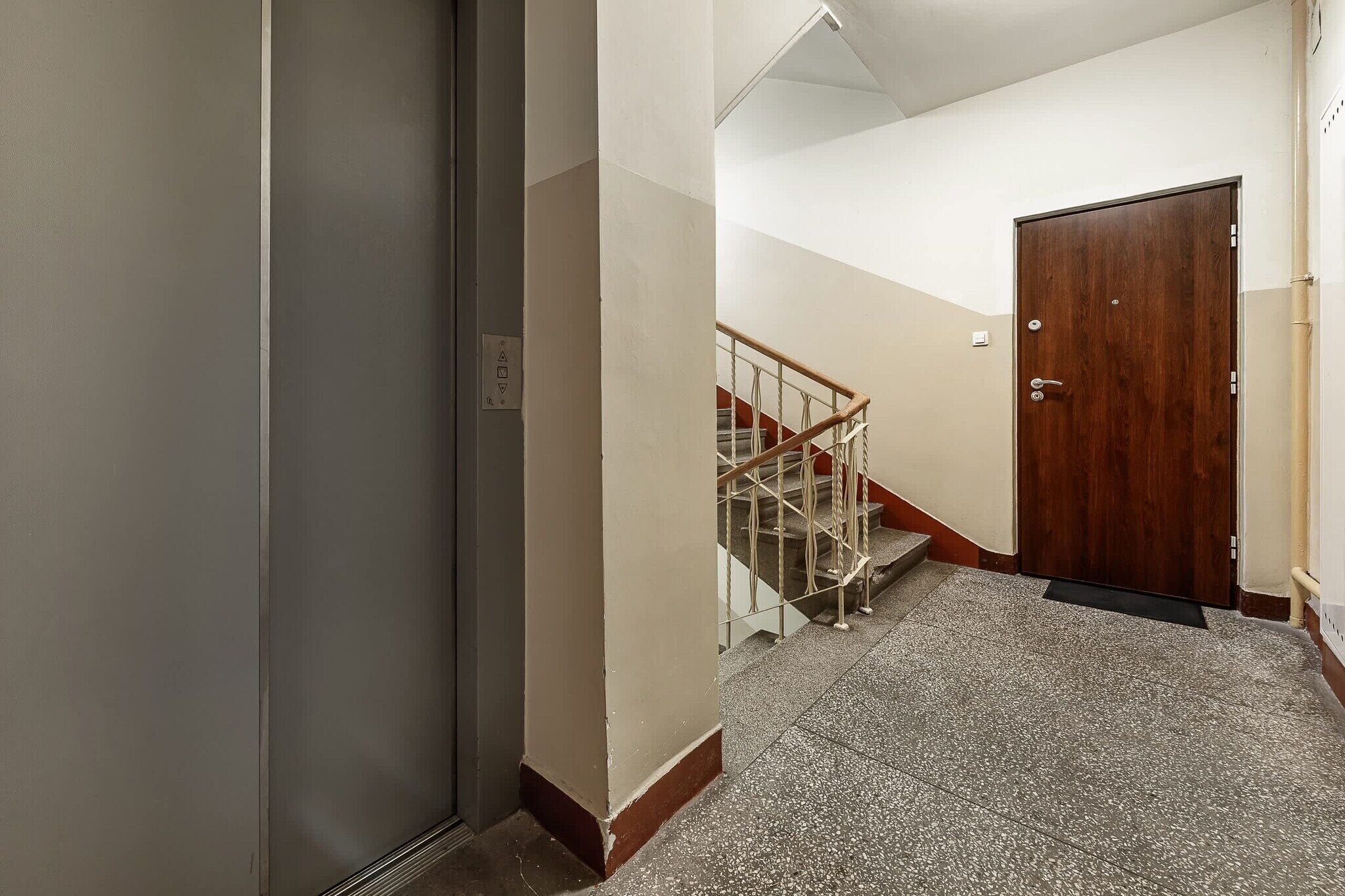 Un pasillo con una puerta de madera, una escalera con barandilla de metal y suelo alfombrado.