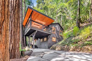 A modern house with a wooden deck, a staircase leading to a balcony, and a stone wall.