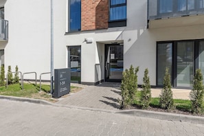 A modern building entrance with a paved pathway leading to a door, a signboard, and a small garden area with shrubs. - Ground-Floor Apartment Stay with Garden Terrace (Łódź)