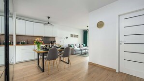 Eine moderne Küche mit weißen Schränken, einem Esstisch mit Stühlen und einer Wohnbereich mit einer Couch und einem grünen Vorhang.
