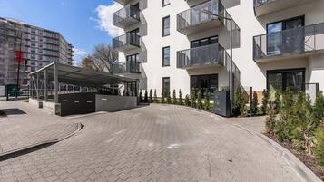 Een modern gebouw met een overdekte ingang, een verhard pad en een rij kleine bomen.