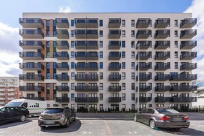 A multi-story residential building with balconies, a parking area with cars, and a clear sky. - Ground-Floor Apartment Stay with Garden Terrace (Łódź)