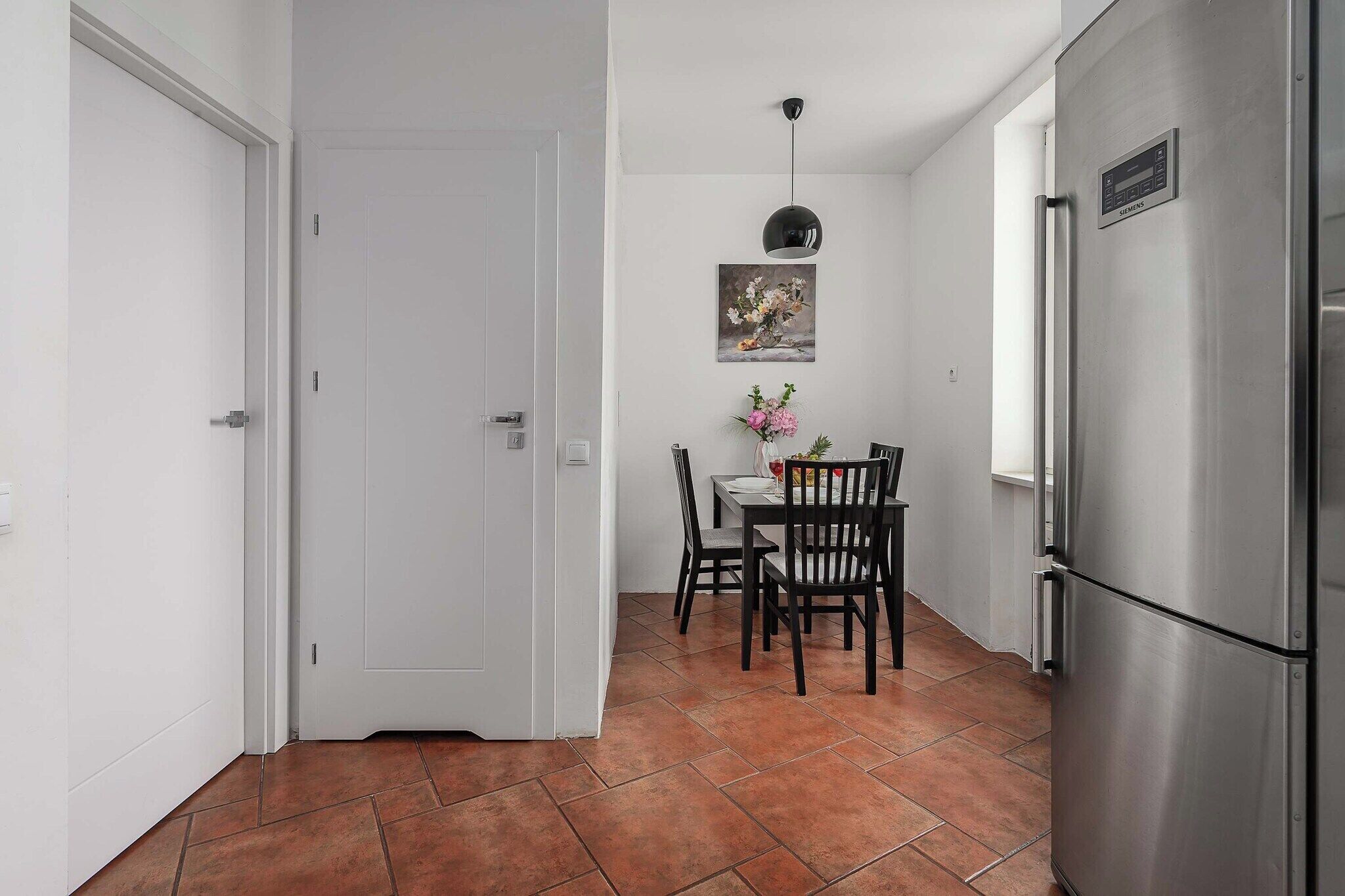 A compact kitchen with a dining area, white walls, a tiled floor, and a stainless steel refrigerator.
