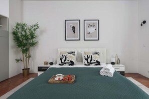 A neatly arranged bedroom with a bed, pillows, a bedside table, a lamp, a potted plant, and two framed artworks on the wall. - Warsaw stay near shops (Warszawa)