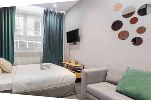 Une chambre d’hôtel avec un lit, un canapé, un téléviseur fixé au mur et une table de chevet avec une horloge et une lampe.
