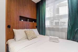 Ein Hotelzimmer mit einem Bett, einem Holzkopfstück, einem Regal mit Dekoration und Blick durch durchscheinende Vorhänge.