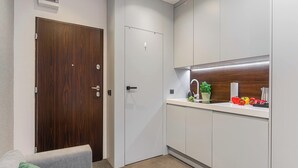 A compact kitchen with a wooden door, white cabinets, a countertop with a sink, and a small potted plant. - Modern Apartment Stay Near Paris (Warszawa)