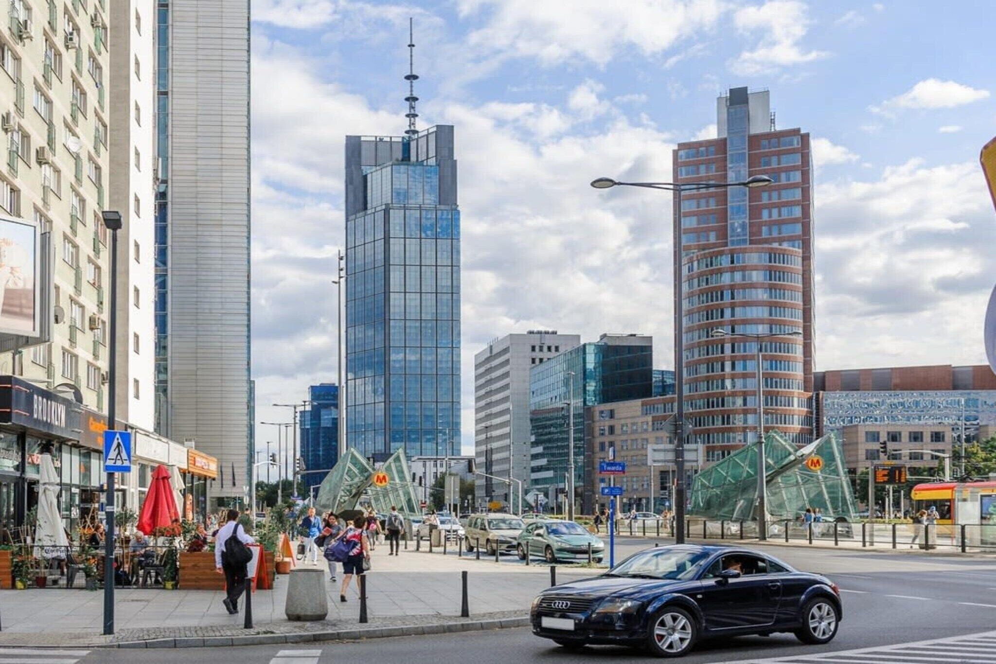 A city street with modern buildings, a pedestrian crossing, and a car driving.
