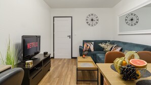 Een moderne woonkamer met een televisie waarop 'NETFLIX' staat, een bank, een salontafel en een schaal met fruit.