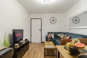 A modern living room with a television displaying 'NETFLIX,' a sofa, a coffee table, and a fruit bowl. - Mansion Haven in Lannilis for 8 (Łódź)