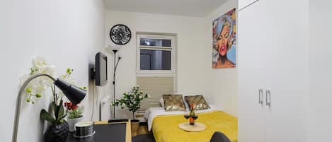 A compact bedroom with a bed, bedside table, lamp, and a painting on the wall.