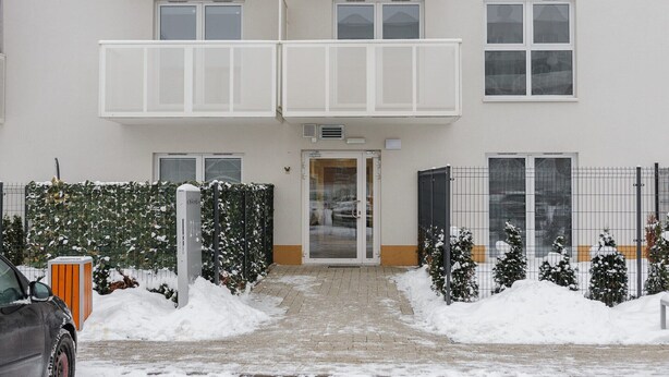Een meerlaags gebouw met een centrale ingang, een omheind gebied met sneeuw, en een geparkeerde auto.