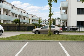A residential area with modern apartment buildings, a paved parking area, and a car parked on the street. - Stylish Urban Apartment for 6 Guests in Łódź (Łódź)