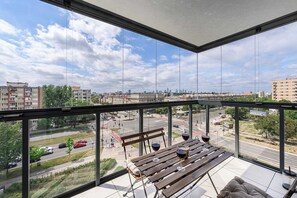 A balcony with a view of a cityscape, a wooden table with glasses of red wine, and a bench. - Family Apartment with Balcony in Warsaw (Warszawa 2)
