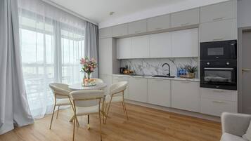 Uma cozinha moderna com armários brancos, uma área de refeições com mesa redonda e cadeiras, e vista para a cidade através de grandes janelas.