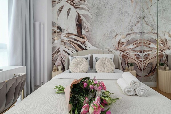 Ein Schlafzimmer mit einem großen Bett, einem Nachttisch, einem Spiegel und einer Wand mit Blättermotiv.