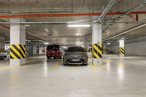 Eine mehrgeschossige Tiefgarage mit Betonpfeilern, gelb-schwarz gestreiften Sicherheitshinweisen und parkenden Fahrzeugen in zugewiesenen Stellplätzen.
