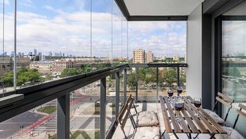 Uma varanda com vista para a cidade, uma mesa com copos de vinho tinto e um banco acolchoado.