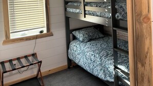 Een stapelbed met beddengoed met een patroon, een raam met zonwering en een klein tafeltje met een kabel.