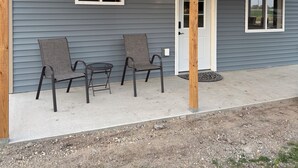 Een huis met een overdekte veranda, twee stoelen en een bijzettafeltje.