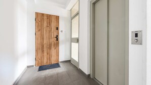 Um corredor com uma porta de madeira, uma porta de correr de vidro e um painel de controle fixado na parede.