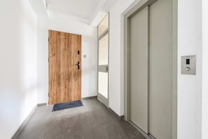 Ein Flur mit einer Holztür, einer Schiebetür aus Glas und einer an der Wand montierten Steuerung.