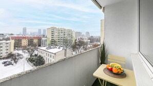 Uma varanda com vista para a cidade, uma mesa com frutas e uma cadeira.