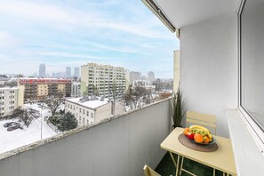 Ein Balkon mit Blick auf eine Stadtansicht, ein Tisch mit Obst und ein Stuhl.