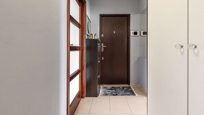 Um corredor com uma porta de madeira, um tapete pequeno e chão de azulejos.