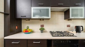 Uma cozinha moderna com armários escuros, fogão a gás, chaleira e uma tigela de frutas.