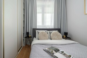 A bedroom with a bed, two bedside lamps, a window with curtains, and a magazine on the bed. - New house with pool near Beach (Warszawa 2)