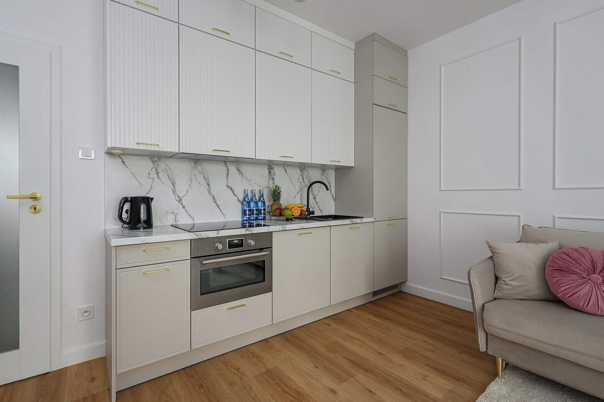 A modern kitchen with white cabinets, a built-in oven, and a countertop with a kettle and fruit.
