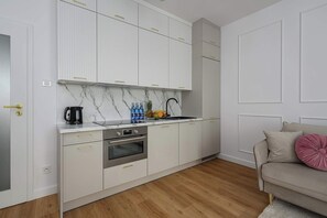 A modern kitchen with white cabinets, a built-in oven, and a countertop with a kettle and fruit. - New house with pool near Beach (Warszawa 2)