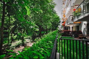 A courtyard with dense greenery, a pathway, and a building with balconies. - City Apartment for 6 guests (Warszawa)