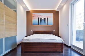 Ein modernes Schlafzimmer mit einem Holzbett, einem großen Fenster und einem Sonnenuntergangsbild an der Wand.