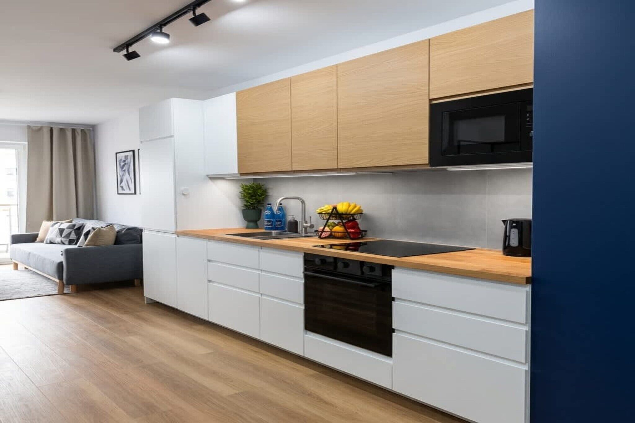 A modern kitchen with white cabinetry, a black microwave, and a wooden countertop.