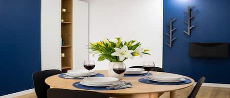A dining area with a round table set for two, a vase of flowers, and a bookshelf in the background.