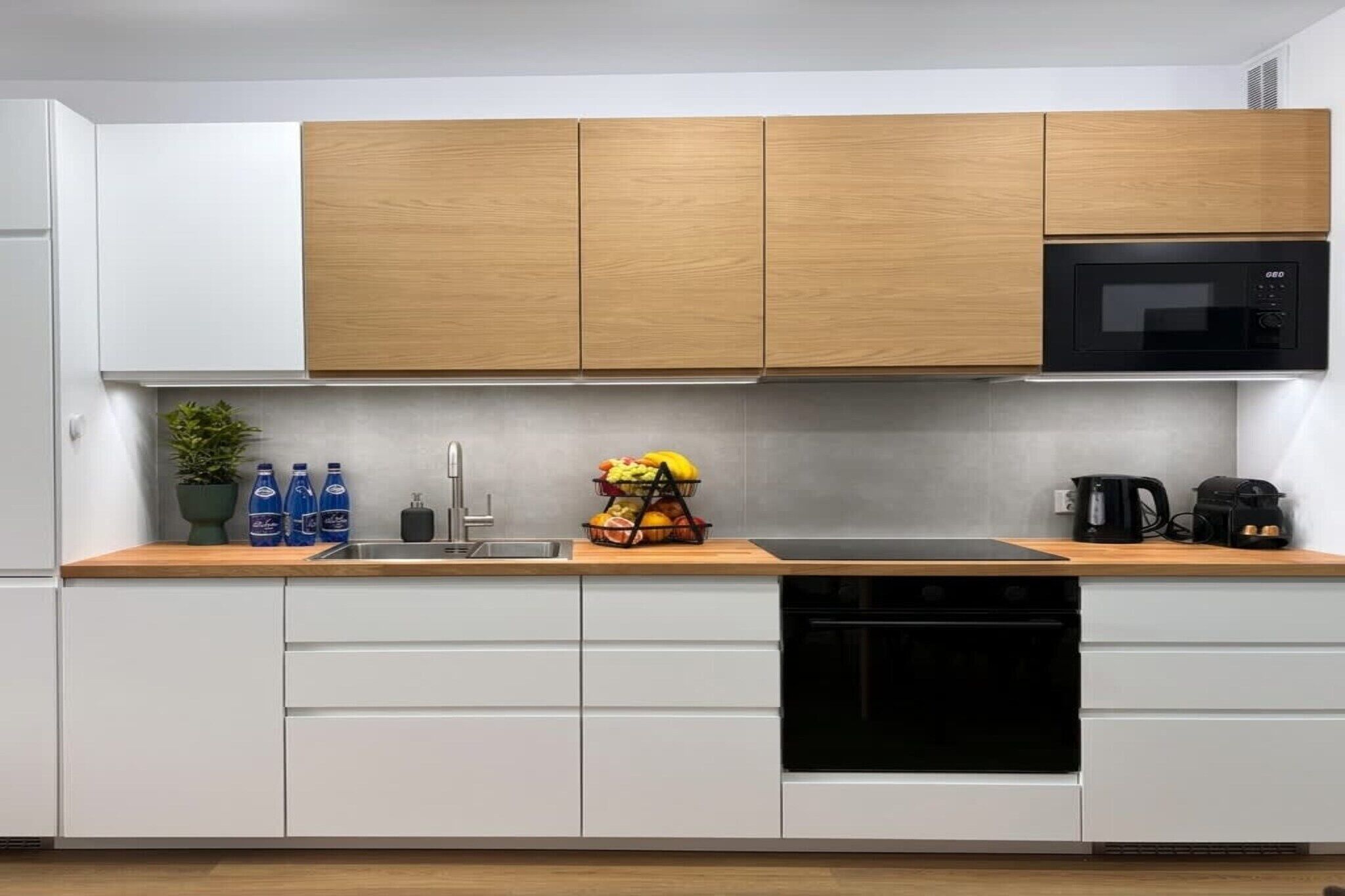 Una cocina moderna con armarios blancos, encimera de madera, microondas negro y una cesta de frutas.