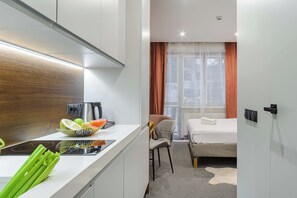 Ein kompaktes Hotelzimmer mit Küchenzeile, einem Bett und einem Fenster mit Vorhängen.