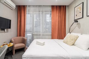 Ein Hotelzimmer mit Bett, Stuhl, Fernseher und einem fenster mit Vorhängen.