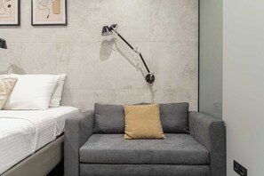 Ein modernes Schlafzimmer mit einem Bett, einem grauen Sofa, einer Stehlampe und einem an der Wand befestigten Regal.